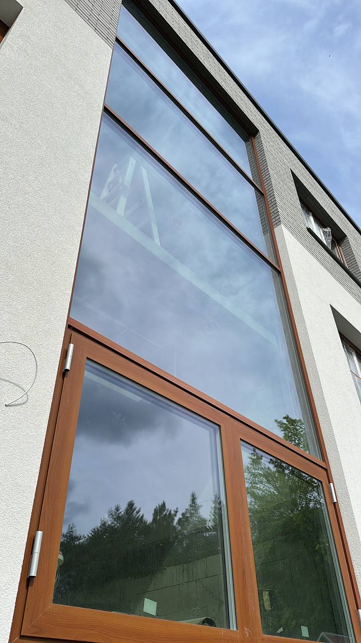 Wysokie przeszklenie fasadowe z drewnianą stolarką okienną w nowoczesnym budynku wielorodzinnym