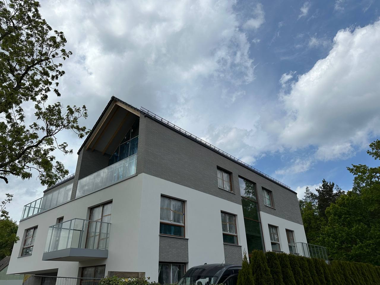 Nowoczesny budynek wielorodzinny z jasną elewacją, szklanymi balustradami balkonowymi i drewnianą stolarką okienną