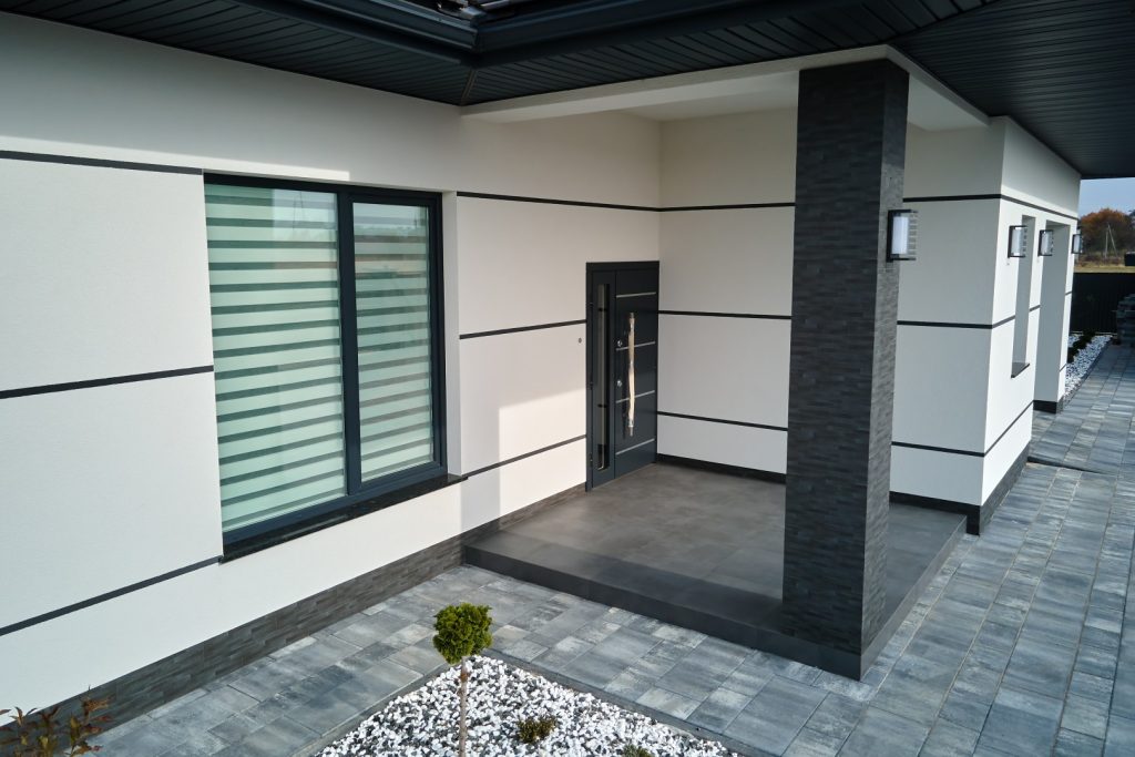 Nowoczesne drzwi zewnętrzne i okna aluminiowe w antracytowym kolorze przy eleganckim wejściu do domu jednorodzinnego