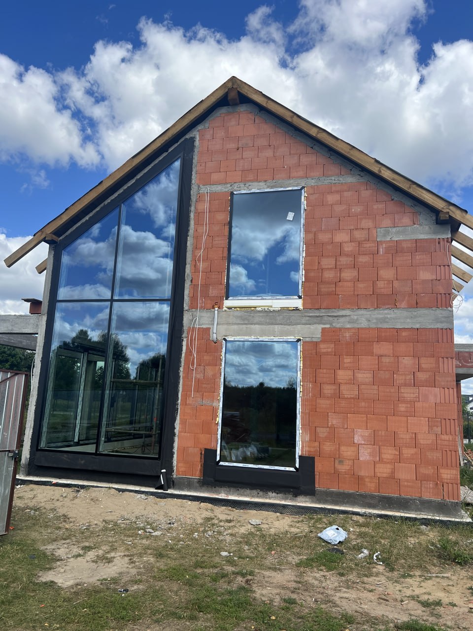 Dom jednorodzinny w budowie z dużą fasadą aluminiowo-szklaną, oknami pionowymi i nowoczesną stolarką okienną