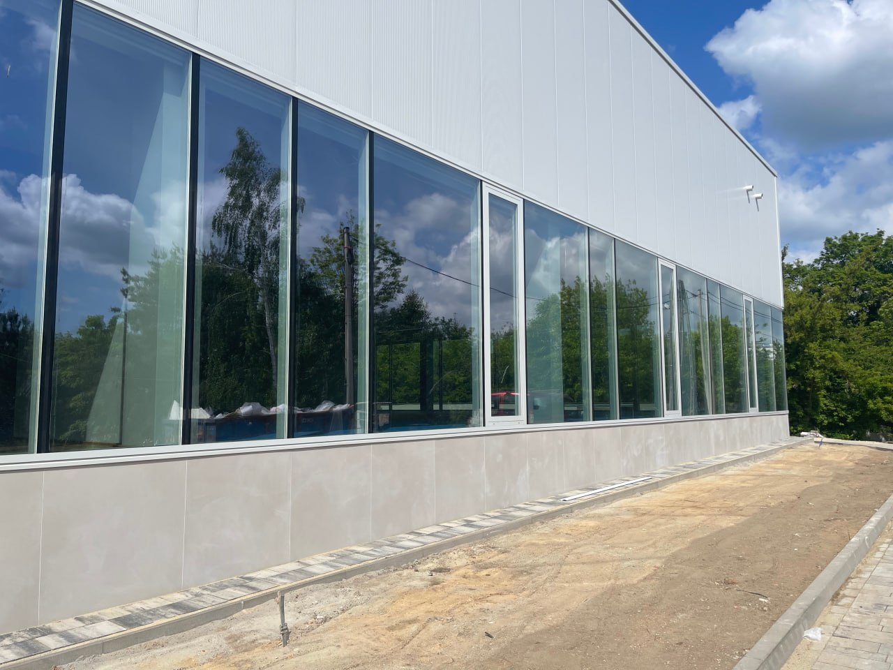 Fasada aluminiowo-szklana w nowoczesnym budynku usługowym z wysokimi przeszkleniami i odbiciem drzew w szybach